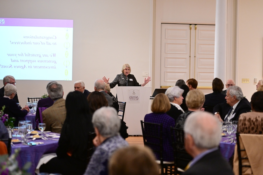 An important person stands a podium in front of a large group of people seated a tables